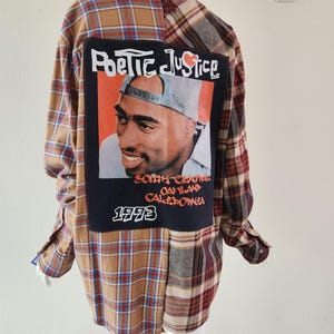 May include: A plaid flannel shirt in brown, tan, and burgundy, featuring a large patch with the text "Poetic Justice" and a portrait of a man. The patch also includes the text "South Central Oakland California 1993".
