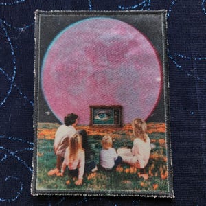 May include: A vintage-style embroidered patch featuring a pink planet, four figures sitting in front of a television with an eye on the screen, and a grassy field.