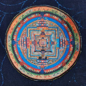May include: A circular mandala patch with intricate details in shades of blue, red, orange, and yellow. The mandala features a square design with multiple layers, surrounded by a circular border with text in a foreign language.