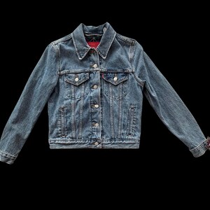 May include: A classic denim jacket in a medium wash blue. The jacket features a collared neckline, button-down front, chest pockets, and side pockets. The sleeves are long, and the cuffs are buttoned. The jacket is a timeless piece of outerwear.