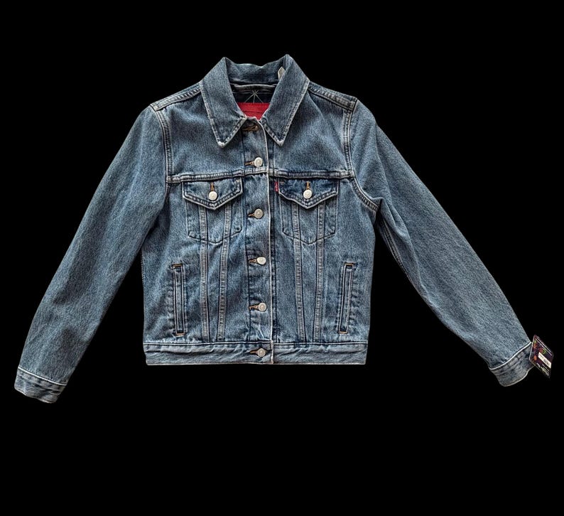 May include: A classic denim jacket in a medium wash blue. The jacket features a collared neckline, button-down front, chest pockets, and side pockets. The sleeves are long, and the cuffs are buttoned. The jacket is a timeless piece of outerwear.
