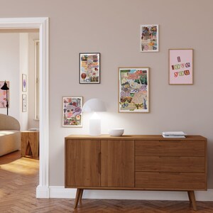 May include: A wooden dresser with three drawers and two doors. The dresser is in a room with a light brown wood floor and white walls. There are several framed pictures on the wall, including one with the words "I love you" in colorful letters.