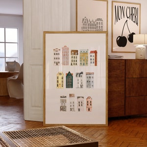 Peut inclure: Une impression encadrée d'une illustration aquarelle de maisons colorées avec des bordures blanches. L'impression est sur fond blanc et est encadrée dans un cadre en bois naturel. L'impression est accrochée à un mur blanc.