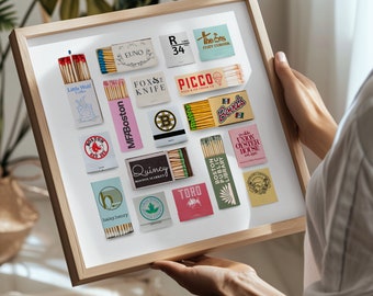May include: A framed collection of 17 matchbox labels featuring various Boston-themed designs. The labels are arranged in a grid pattern and include names like "Little Wolf Coffee", "MFABoston", "Quincy Boston Market", "Toro", "Boston Public Library", "The Sts Cozy Corner", "Picco Pizza & Ice Cream Co", and "Bova's".