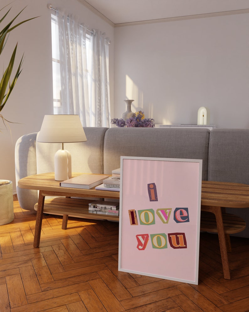 May include: A framed print with a pink background and white frame. The print features the words "i love you" in colorful, cut-out letters.