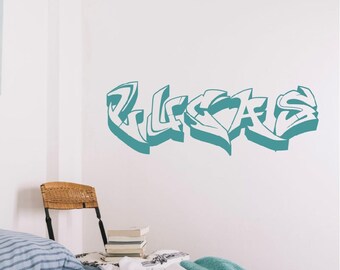 May include: A teal graffiti-style wall decal featuring the name LUCAS in bold, stylized lettering. The design consists of sharp, angular characters with a three-dimensional effect, applied directly to a plain white wall surface.