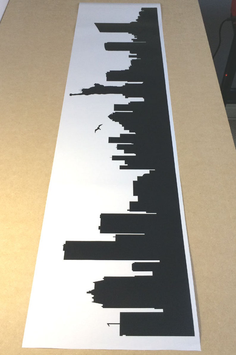 May include: A long, rectangular white decal featuring a black silhouette of the New York City skyline. The design includes various skyscrapers, the Statue of Liberty, and a single bird in flight, all rendered in a solid, high-contrast black graphic.