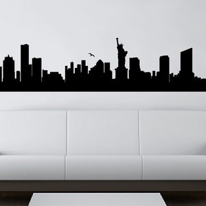 May include: A black wall decal featuring a detailed silhouette of the New York City skyline, including various skyscrapers and the Statue of Liberty. A small bird is depicted in flight above the buildings, creating a wide, horizontal graphic.