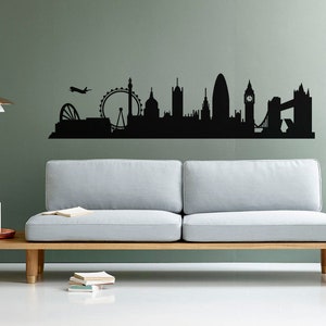 May include: A black wall decal featuring a silhouette of the London skyline, including the London Eye, St. Paul's Cathedral, the Gherkin, Big Ben, and Tower Bridge, with a small airplane flying above the city structures on a solid wall.