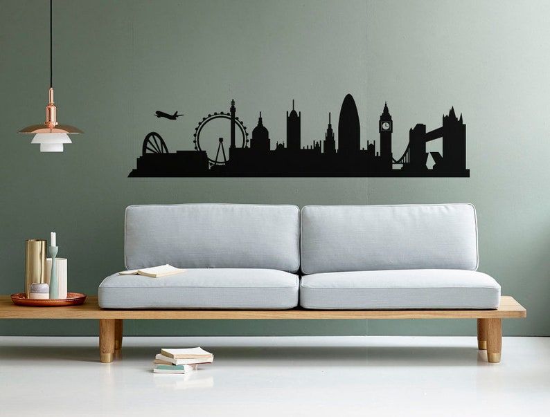 May include: A black wall decal featuring a silhouette of the London skyline, including the London Eye, St. Paul's Cathedral, the Gherkin, Big Ben, and Tower Bridge, with a small airplane flying above the city structures on a solid wall.