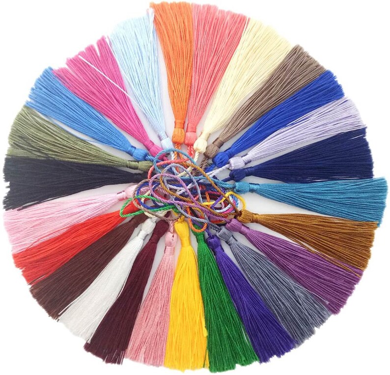 K&ouml;nnte beinhalten: Eine Sammlung von 24 bunten Quasten, jede in einer anderen Farbe, darunter Rot, Blau, Gr&uuml;n, Gelb, Lila, Orange, Braun, Schwarz, Wei&szlig; und Rosa. Die Quasten sind in einem Kreis angeordnet, wobei die Spitzen der Quasten nach au&szlig;en zeigen.