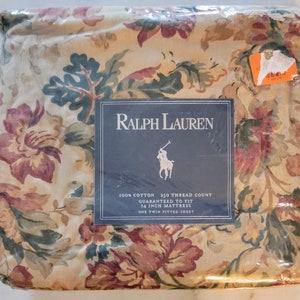 May include: A twin-sized fitted sheet in a floral pattern with a beige background, green leaves, and red and brown flowers. The sheet is packaged in plastic and has a label that reads "Ralph Lauren 100% Cotton 250 Thread Count Guaranteed to Fit 14 Inch Mattress One Twin Fitted Sheet."