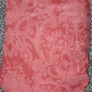 May include: A red fabric with a white floral pattern. The pattern features intricate swirls and leaves.