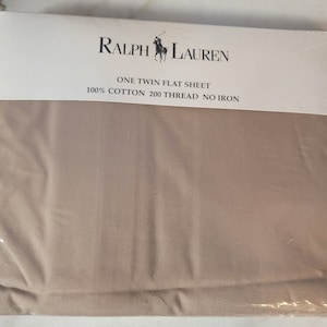 May include: A beige twin flat sheet made of 100% cotton with a 200 thread count. The sheet is labeled "Ralph Lauren" and "One Twin Flat Sheet 100% Cotton 200 Thread No Iron".
