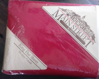 May include: A red King Flat Sheet from Main Street by Stevens. The sheet is packaged in plastic and has a white label with the text "King Flat Sheet No Iron Percale".