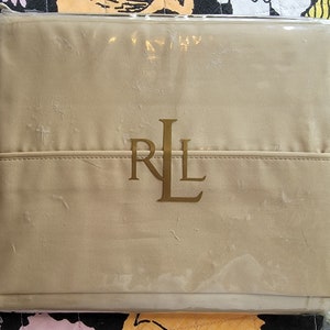 May include: A beige fitted sheet with a gold embroidered "RL" logo in a plastic packaging.