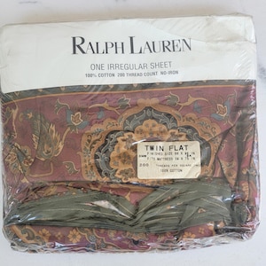 May include: A Ralph Lauren twin flat sheet in its original packaging. The sheet features a floral pattern in shades of burgundy, green, and gold. The packaging includes the text "ONE IRREGULAR SHEET" and "100% COTTON". The sheet measures 66 x 98 inches.