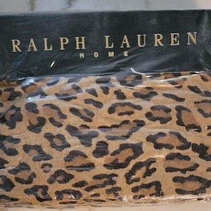 May include: A packaged bed sheet set with a leopard print design. The sheets are tan with dark brown and black spots. The packaging has the words "RALPH LAUREN HOME" in gold lettering on a black background.