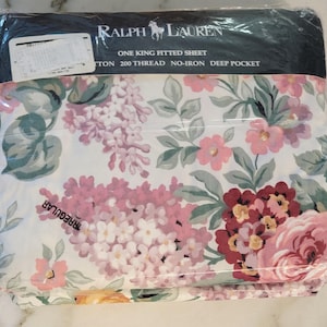 May include: A packaged Ralph Lauren One King fitted sheet. The sheet features a floral pattern with pink, red, and purple flowers, along with green leaves, on a white background. The packaging includes the brand name and product details.