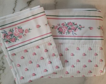 May include: A set of two white cotton pillowcases with a pink and green floral pattern. The pillowcases have a striped pattern with small pink roses.