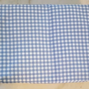 May include: Folded fabric with a blue and white gingham pattern. The fabric is a light blue color with a classic checkered design. The fabric is folded neatly, showing the pattern clearly.