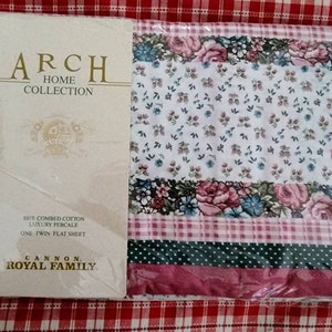 May include: A white twin flat sheet with a floral pattern in shades of pink, blue, and green. The sheet is packaged in plastic and has a label that reads "Arch Home Collection" and "Cannon Royal Family".