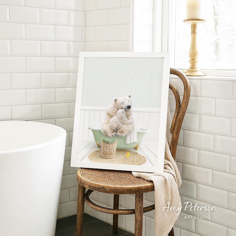 A framed image of a polar bear sitting in a bathtub, with a basket of toys nearby, is displayed on a wooden chair in a bathroom setting.