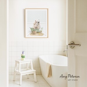 A framed image of a polar bear sitting in a bathtub is displayed on the wall above a white bathtub in a bathroom.