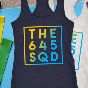 May include: Navy and grey racerback vests with the text "THE 645 SQD" in a square. The text is gradient yellow to blue. Also shown are blue, yellow, and green resistance bands, and a pink camo foam roller.