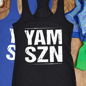 May include: Black and blue racerback vests with the text "YAM SZN" in white. The image also includes a blue sports bra, resistance bands, and decorative geometric light fixtures.