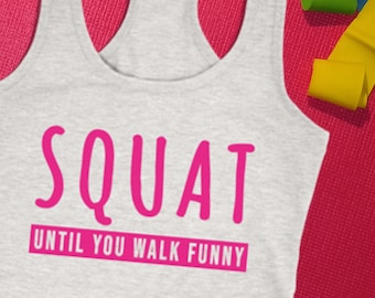 Puede incluir: Una camiseta sin mangas gris claro con la palabra "SQUAT" en rosa brillante y la frase "UNTIL YOU WALK FUNNY" en un rectángulo rosa. La camiseta sin mangas está sobre una esterilla de yoga rosa, con bandas de ejercicio.