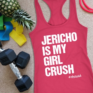Puede incluir: Una camiseta sin mangas roja con el texto "Jericho is my girl crush" en blanco. La imagen también incluye una piña, pesas, bandas de resistencia y una cuerda para saltar.
