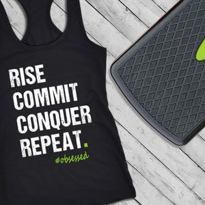 May include: Black racerback tank top with the words "RISE COMMIT CONQUER REPEAT" in white block letters. The word "#obsessed" is in green below the text. A black exercise step is in the background.