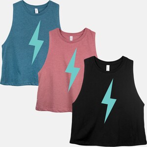 May include: Three sleeveless crop tops in teal, dusty rose, and black. Each top features a large turquoise lightning bolt graphic on the front. The tops have a rounded neckline and a relaxed fit, suitable for casual wear or workouts.