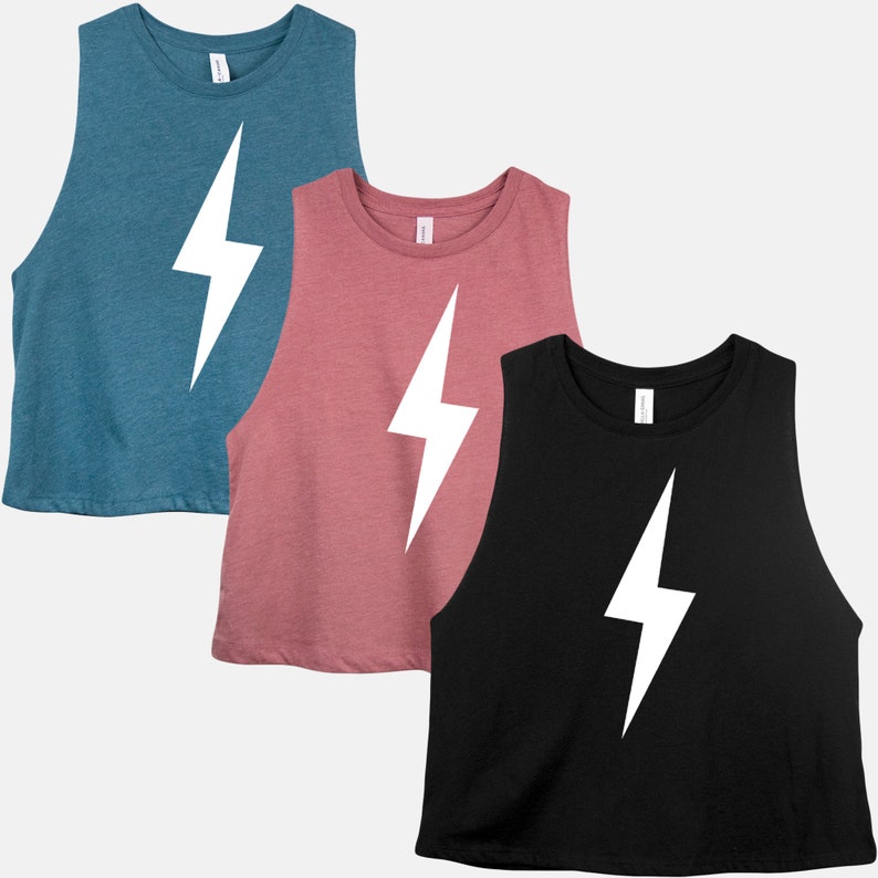 May include: Three sleeveless crop tops in teal, dusty rose, and black. Each top features a large white lightning bolt graphic on the front. The tops have a rounded neckline and a slightly cropped fit, suitable for casual wear.
