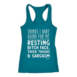 May include: Teal racerback tank top with white text that reads "THINGS I HAVE GOING FOR ME RESTING BITCH FACE, THICK THIGHS & SARCASM" with the hashtag "#obsessed". The tank top has a scoop neck and a racerback design.
