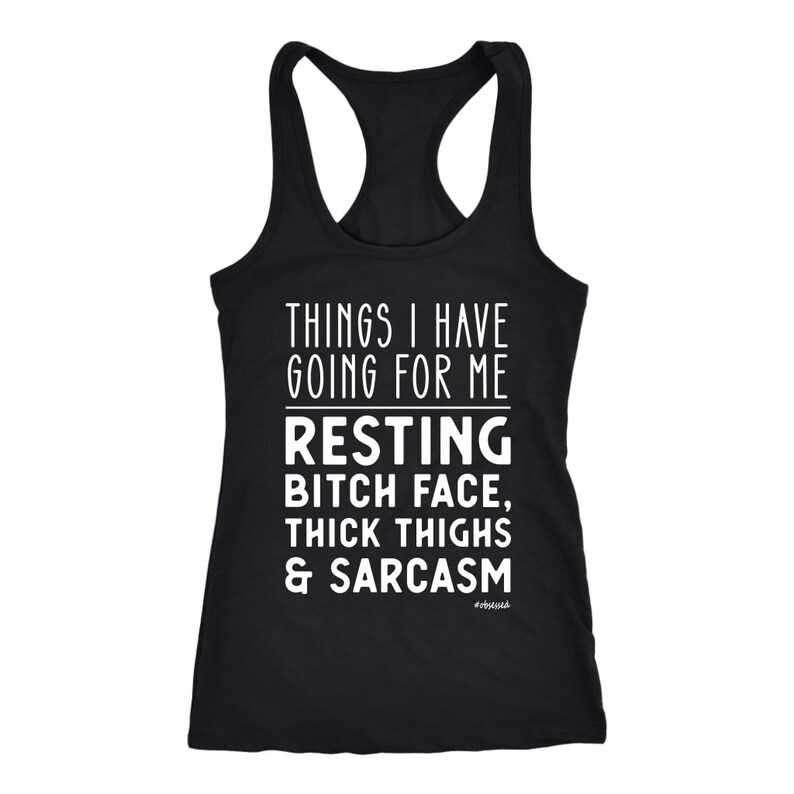 May include: Black racerback tank top with white text that reads "THINGS I HAVE GOING FOR ME RESTING BITCH FACE, THICK THIGHS & SARCASM." The word "#obsessed" is printed below the text.