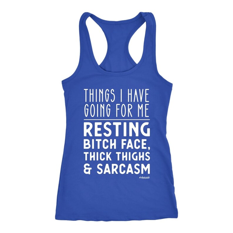 May include: A royal blue racerback tank top with white text. The text reads "THINGS I HAVE GOING FOR ME" above "RESTING BITCH FACE, THICK THIGHS & SARCASM". The word "OBSESSED" is at the bottom.