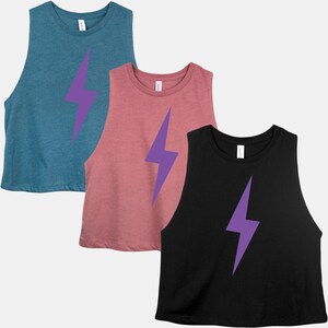 May include: Three sleeveless crop tops in teal, dusty rose, and black. Each top features a large purple lightning bolt graphic on the front. The tops are made of a soft, lightweight material, suitable for workouts or casual wear.