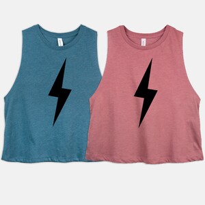 May include: Two sleeveless crop tops, one teal and one dusty rose, each with a large black lightning bolt graphic. The tops have a scoop neck and a relaxed fit, suitable for casual wear.