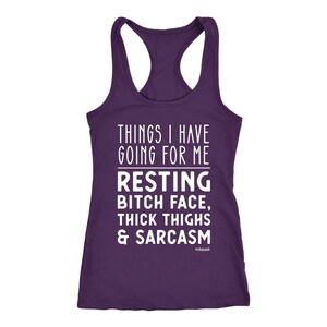 May include: A purple racerback tank top with white text. The text reads "THINGS I HAVE GOING FOR ME" above "RESTING BITCH FACE, THICK THIGHS & SARCASM". The word "#obsessed" is at the bottom.