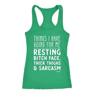 May include: A green racerback tank top with white text. The text reads "THINGS I HAVE GOING FOR ME RESTING BITCH FACE, THICK THIGHS & SARCASM". The word "#obsessed" is at the bottom.