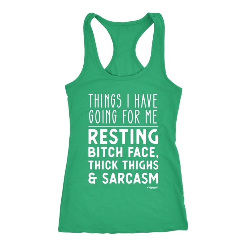 May include: A green racerback tank top with white text. The text reads "THINGS I HAVE GOING FOR ME RESTING BITCH FACE, THICK THIGHS & SARCASM". The word "#obsessed" is at the bottom.