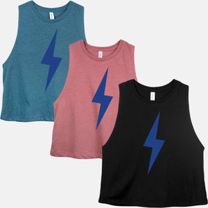 May include: Three sleeveless crop tops in teal, dusty rose, and black. Each top features a large blue lightning bolt graphic on the front. The tops have a crew neck and are made of a soft material.