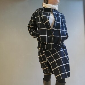 May include: A navy blue and white grid-patterned jacket and skirt set. The jacket is open, revealing a white top. The skirt is a wrap style. The outfit is paired with black boots.