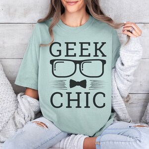 May include: A light blue t-shirt with the text "GEEK CHIC" in black. The text is surrounded by a pair of black glasses and a black bow tie.