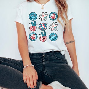 May include: White t-shirt with a red, white, and blue peace sign, smiley face, and star design.