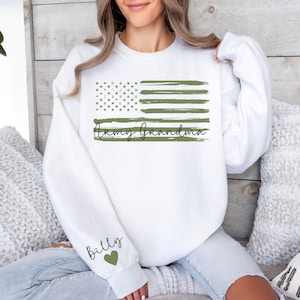 May include: White sweatshirt with a green and white American flag design and the text "Army Grandma". The left sleeve has the text "Billy" with a green heart.