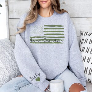 May include: Gray sweatshirt with a green and white American flag design and the text "Army Grandma". The left sleeve has the text "Billy" with a heart.