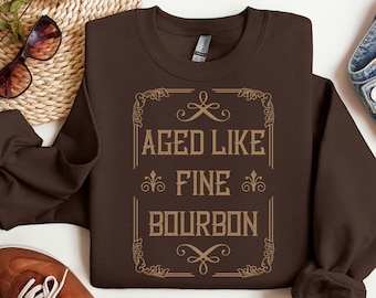 May include: Brown sweatshirt with a vintage-style graphic that says "Aged Like Fine Bourbon".